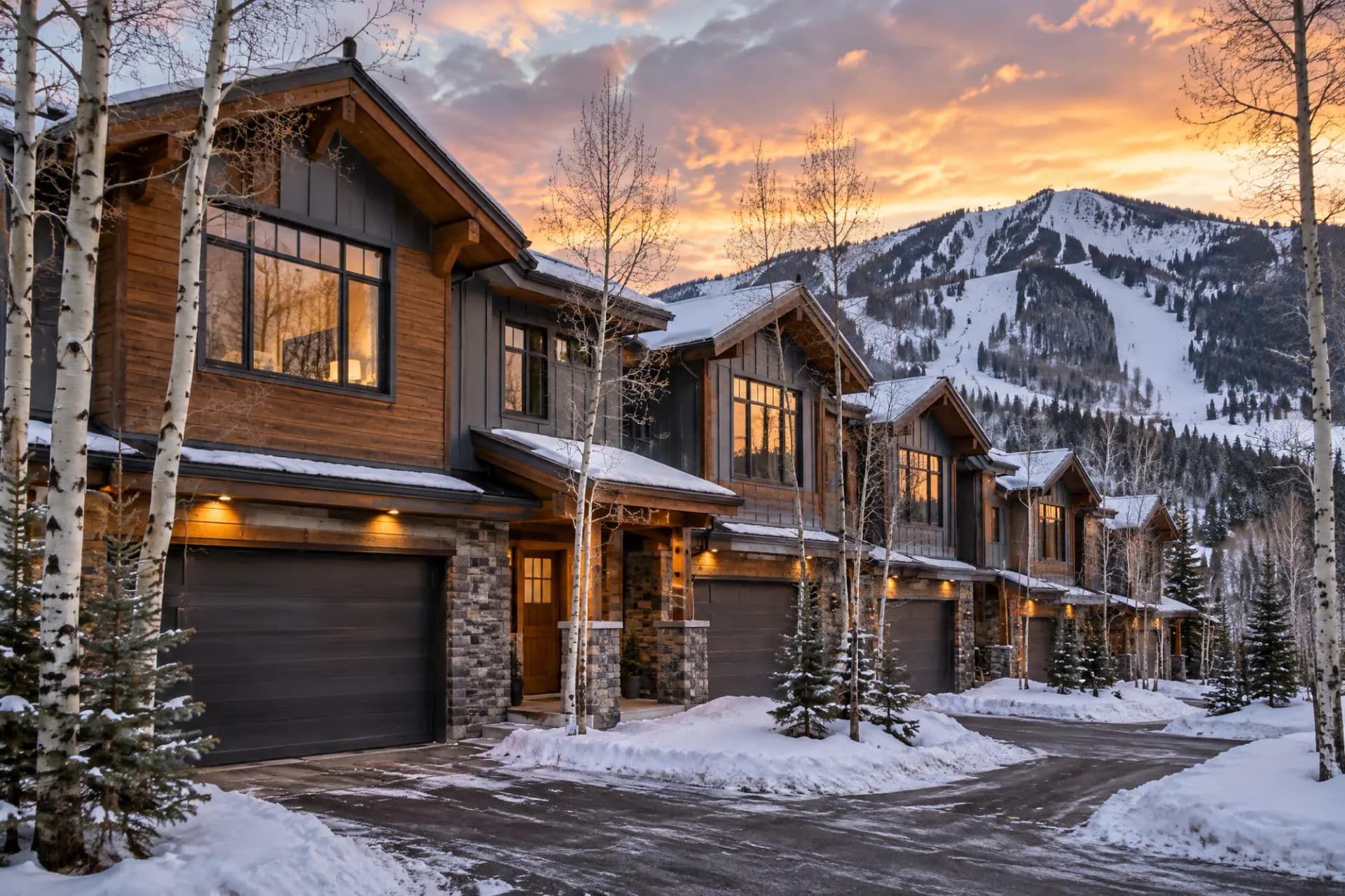 A row of mountain townhomes with a ski mountain behind them at sunset